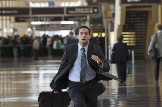 A businessman in formal attire rushing through an airport terminal, possibly late for a flight.