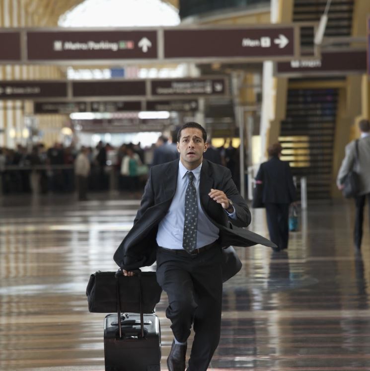 A businessman in formal attire rushing through an airport terminal, possibly late for a flight.